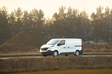 Kırsal yolda beyaz minibüs sürüyor.