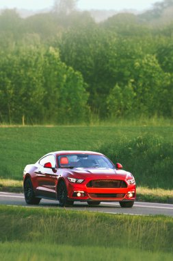 Kırsaldan geçen parlak kırmızı bir araba.