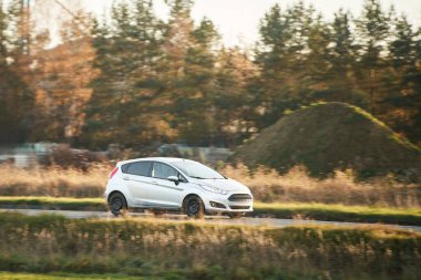 Kırsal yolda beyaz hibrit araba sürüyor.