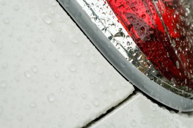 Beyaz metal panelli kırmızı fren lambalarına yağmur damlaları düşer.