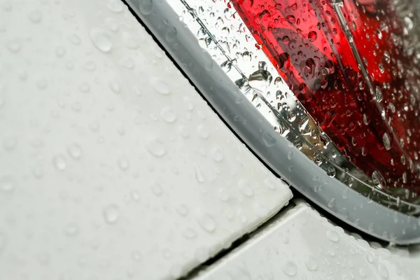 Beyaz metal panelli kırmızı fren lambalarına yağmur damlaları düşer.