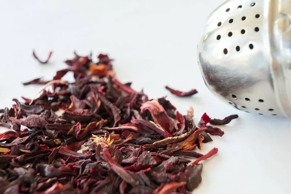 Close up of loose hibiscus tea leaves and tea ball on white background.