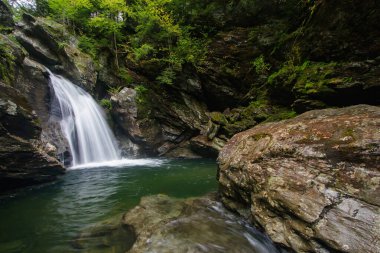 Vermont waterall flows into hidden rocky pool in the forest.