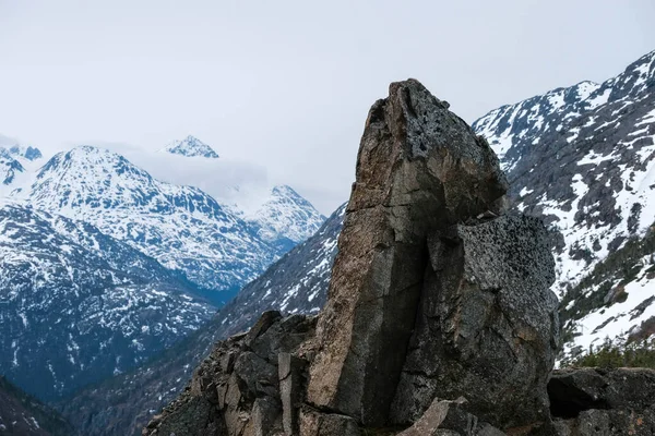 低い雲と雪の山の頂上を持つ大きく険しい石 — ストック写真