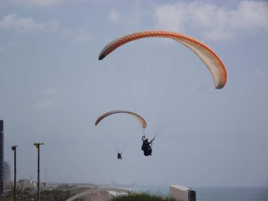 Gökyüzünde yamaç paraşütü yapıyor. Sadece siluet görünüyor. Bir adam kıyı boyunca deniz üzerinde bir paraglider üzerinde uçuyor. Netanya, İsrail