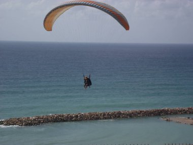 Gökyüzünde yamaç paraşütü yapıyor. Sadece siluet görünüyor. Bir adam kıyı boyunca deniz üzerinde bir paraglider üzerinde uçuyor. Netanya, İsrail