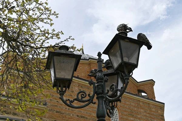 Vintage steel street lamp. A retro street lamp stands in a cozy city courtyard with new modern buildings. Vintage steel street lamp in sun glare, retro lantern. Vintage street lamp post during the day