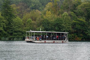 Plitvice Lakes, Hırvatistan - 19 Eylül 2024: Gezi teknesindeki turistler, Plitvice Gölleri Ulusal Parkı 'nın sonbahar manzarası. Yüksek kalite fotoğraf