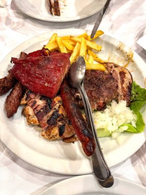 Patates kızartması ve salatayla servis edilen bir tabakta sosis ve birkaç çeşit ızgara et. Yüksek kalite fotoğraf