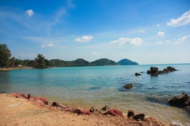 Denizde siyah kayalar Arkasında bir dağ var.