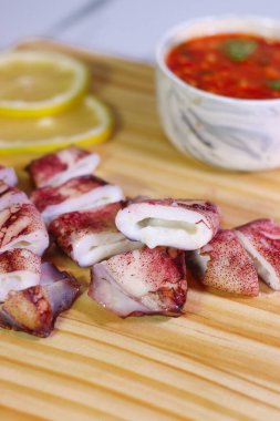 Ahşap tahtada ızgara mürekkep balığı parçaları. Sos ve limon soslu.