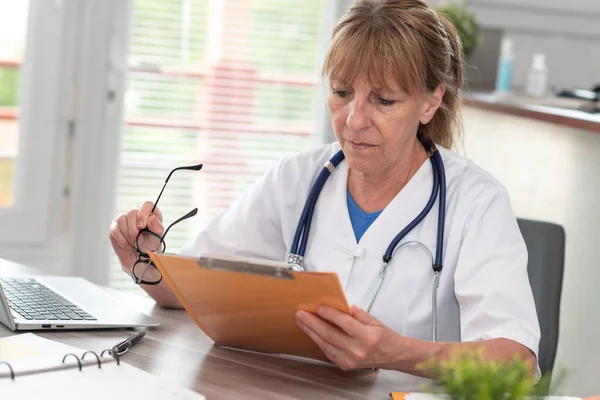 Γυναίκα Γιατρός Που Διαβάζει Ένα Κλινικό Αρχείο Στο Ιατρικό Γραφείο — Φωτογραφία Αρχείου