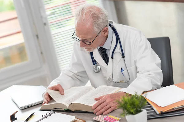 Ανώτερος Γιατρός Διαβάζει Ένα Εγχειρίδιο Στο Ιατρικό Γραφείο — Φωτογραφία Αρχείου