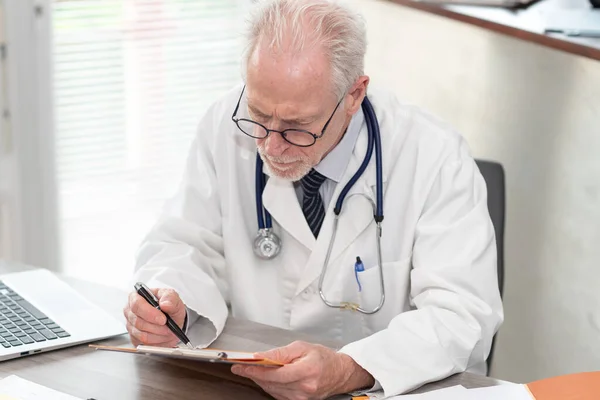 Ανώτερος Γιατρός Που Διαβάζει Ένα Κλινικό Αρχείο Στο Ιατρικό Γραφείο — Φωτογραφία Αρχείου
