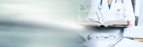 Female doctor reading a medical book at her desk; panoramic banner