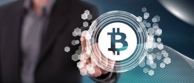 Bir adam dokunmatik ekranda bitcoin konseptine parmağıyla dokunuyor.