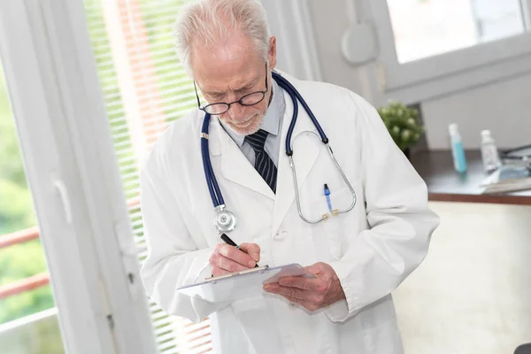 Senior Doctor Taking Notes Clipboard Medical Office — Stockfoto