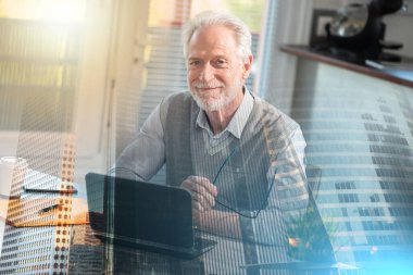 Portrait of smiling senior businessman sitting in office; multiple exposure