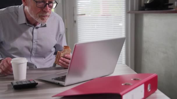 Senior Geschäftsmann Isst Ein Sandwich Während Büro Laptop Arbeitet — Stockvideo