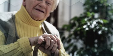 Yaşlı kadın elleri değnekte oturuyor, geometrik desenli.