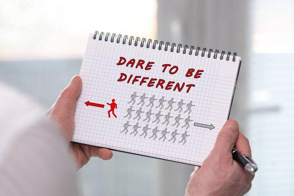 Рука держит блокнот с осмеливаться быть другой концепцией