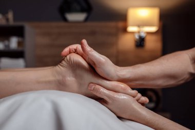 Relaxing foot massage, hands of a female massage therapist massaging female client foot in dark room of massage spa
