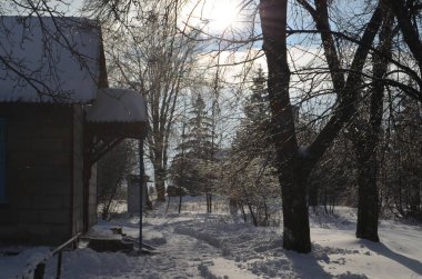 Soğuk bir gün, küçük bir avlu, bir ev, bir veranda, ağaçlar tasvir ediliyor, her şey karla kaplı, güneş bulutların arasından parlıyor..