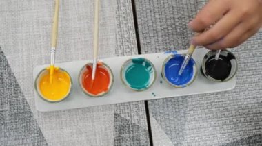 Resim yapmak için boya bardağına batırılmış fırçayı tutan bir elin yakın çekimi. Küçük bir seramik bardakta suluboya tablo üzerinde fırça ile sanat çalışması için. 