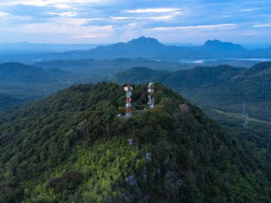 Güzel sabah manzarası, altın gün doğumu ve sisli elektrik direği ve metal yapılarla dolu bulutların üstündeki dağ zirveleri. Teknoloji ve doğa uyum içinde.