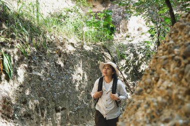 Sırt çantalı bir kadın jeolog ormanda doğa izlerini araştırıyor ve kaya ya da çakıl analizi yapıyor. Araştırmacılar biyolojik materyal örnekleri topluyorlar. Çevre ve ekoloji araştırmaları.