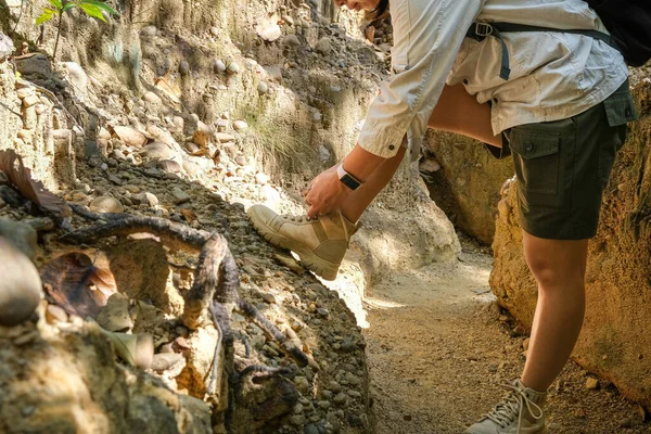 Female geologist tying shoelaces while examining nature, analyzing rocks or pebbles. Researchers collect samples of biological materials. Environmental and ecology research.
