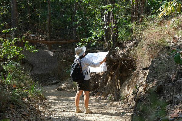 Female geologist using a map, examining a natural path and analyzing rocks or gravel. Researchers collect samples of biological materials. Environmental and ecology research.