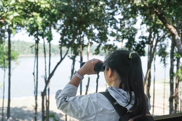Hiker young woman looking birds through binoculars telescope in forest. tourist with backpack watching wild birds through binoculars in the jungle.