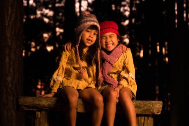 Soğuk havada kamp ateşinin yanında ısınan şirin küçük kız kardeşler. Çocuklar kamp ateşinde eğleniyor. Çocuklarla birlikte kış çam ormanında kamp yapmak. Mutlu aile doğada tatilde..
