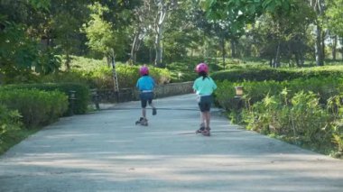 Portrait of active little girl riding scooter on street in outdoor park on summer day. Happy Asian girl wearing a helmet riding a kick scooter in the park. Active leisure and outdoor sport for child.