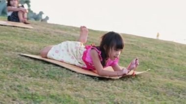 Happy little girl playing at the park slides down from the grassy hill sitting on a cardboard box. Happy children playing outdoors in summer. Family spending time together on vacation.