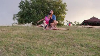 Happy sisters playing at the park slides down from the grassy hill sitting on a cardboard box. Happy children playing outdoors in summer. Family spending time together on vacation.
