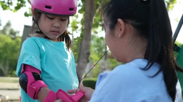 夏の日に屋外公園の路上でアクティブな女の子の乗馬スクーターの肖像画 公園でキックスクーターに乗ってヘルメットをかぶって幸せなアジアの女の子 子供のためのアクティブなレジャーや屋外スポーツ — ストック動画