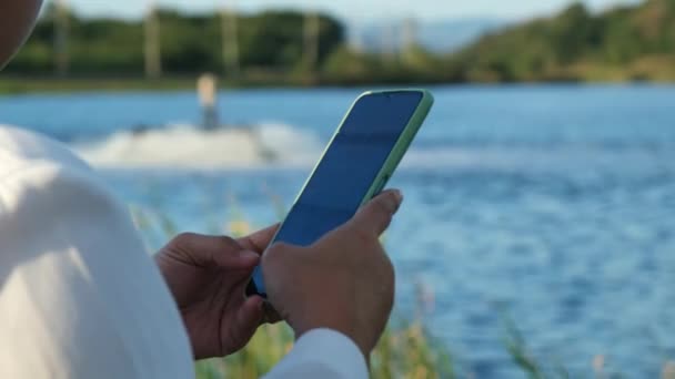 戴着白色头盔的环境工程师使用手机在池塘里操作氧气涡轮曝气机 水和生态概念 — 图库视频影像