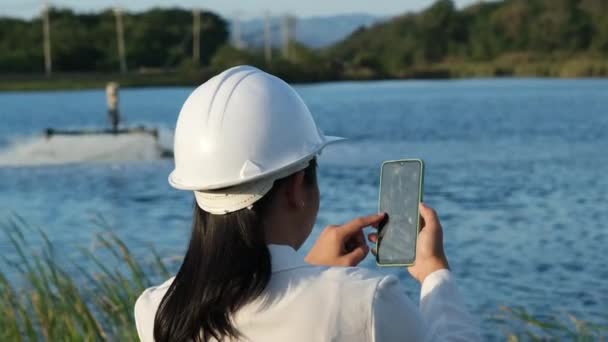 白いヘルメットを着用した環境エンジニアは 携帯電話を使用して池の酸素タービンエアターを操作します 水と生態学の概念 — ストック動画