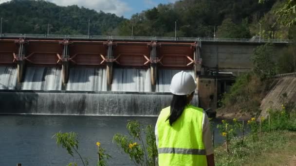 身穿绿色背心 头戴白色头盔的女工程师在水电站和灌溉大坝外工作 可再生能源系统 可持续能源概念 — 图库视频影像
