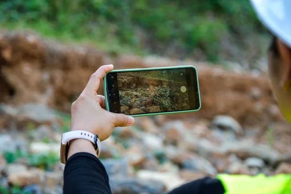 Female geologist using mobile phone to take pictures, examine nature and analyze rocks or pebbles. Researchers collect samples of biological materials. Environmental and ecology research.