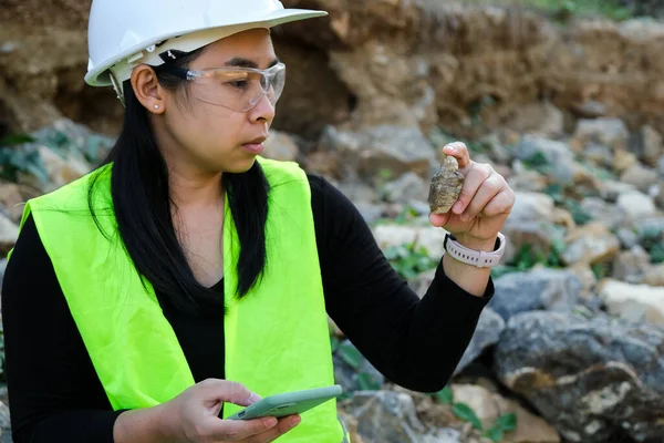Female geologist using mobile phone to record data analyzing rocks or gravel. Researchers collect samples of biological materials. Environmental and ecology research.