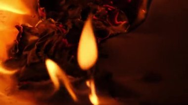 Flames on a burning silver cross blazing in the night. Close up burning paper with silver cross placed in center on black background.