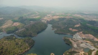 Kuzey Tayland tepelerinde su barajı ve göl rezervuarı panoramik hava manzarası. Dağ gölündeki hava manzarası. Dağ vadisindeki su deposunda yeşil bahar ormanlarıyla kaplı bir dron..