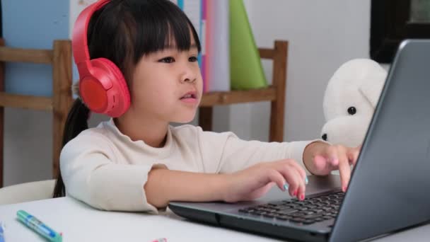 可爱的小学女生戴着耳机 使用笔记本电脑 快乐的亚洲孩子们通过笔记本电脑或在家学习 听音乐或玩游戏 在网上进行互动学习 — 图库视频影像