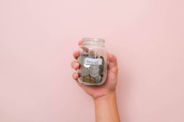 Pembe arka planda içinde para olan cam kavanozu yakın plan. El ele para kavanozu, seyahat, tasarruf, eğitim, bağış. Finans planı konsepti.