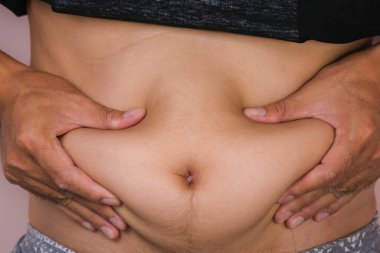 Şişman erkek el, pembe arka planda izole edilmiş göbek yağını tutuyor. Adam şişko karnına dokunuyor. Koca göbekli şişman genç bir adam.