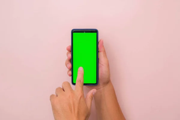 Human hand using mobile smartphone with mockup green screen on pink background. Male hand tapping and pinch to zoom in or zoom out on blank digital screen.