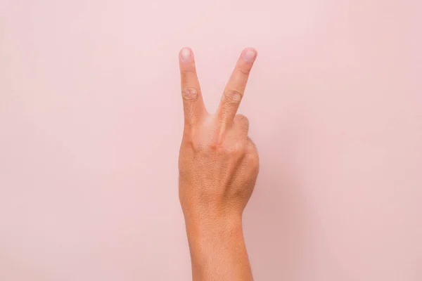 Hand showing two fingers gesture (peace sign) isolated on pink background.